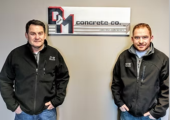 Dan and Sean, co-owners of D&M Concrete, standing in front of the company sign